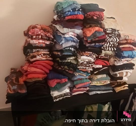 ערימות בגדים מקופלים על שולחן עם שקיות מתחת